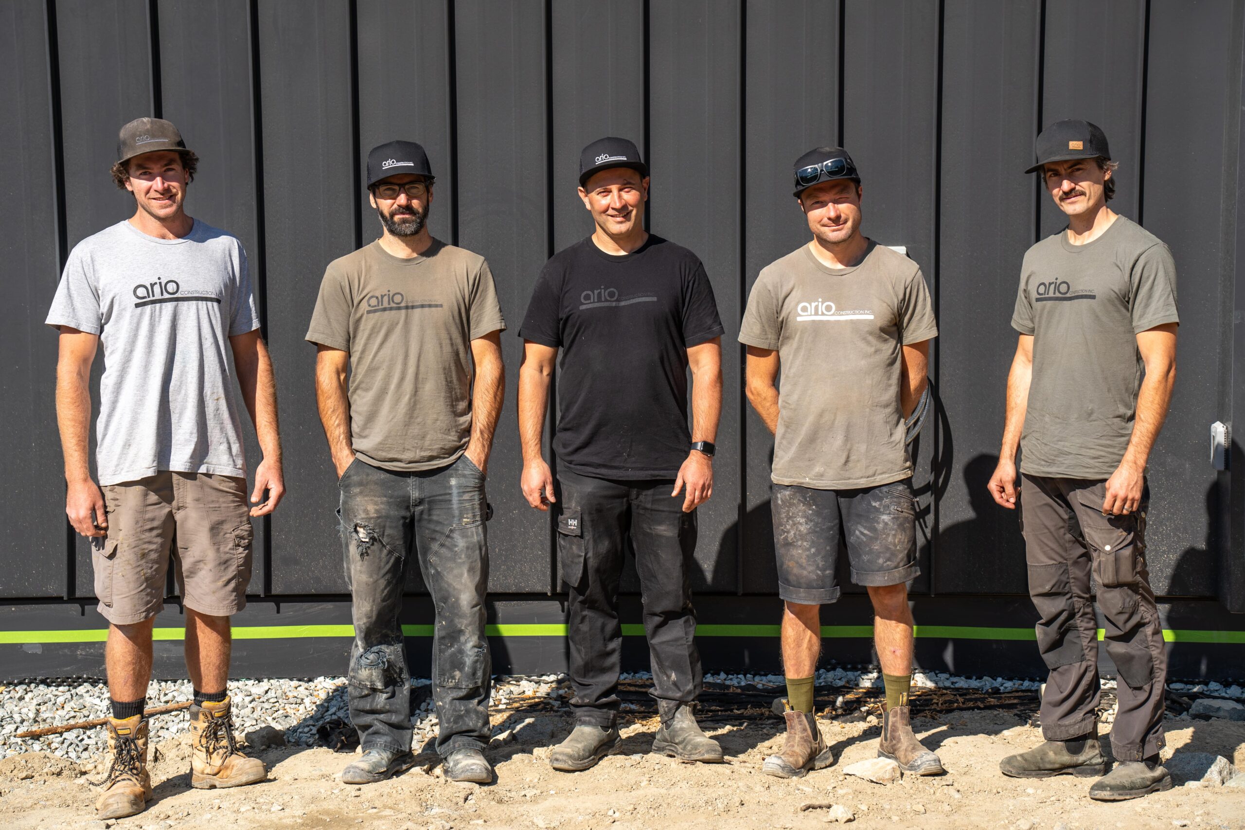 I'd be happy to create SEO-friendly alt text and description for the Ario Construction team image. Here are my suggestions: Alt Text: "Ario Construction Inc. professional team members wearing branded shirts standing in front of a modern construction project in Whistler, British Columbia