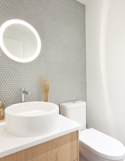 Modern powder room with round mirror and white fixtures in Whistler Passive House
